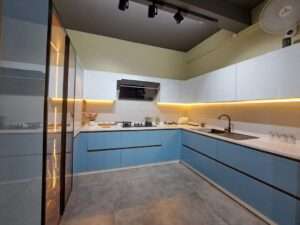 Stylish L-shaped modular kitchen with blue and white cabinets, under-cabinet lighting, and a sleek black chimney.