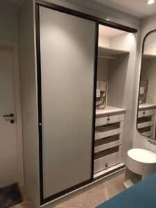 Sleek sliding wardrobe with a frosted glass panel, built-in dresser with drawers, and soft LED lighting.